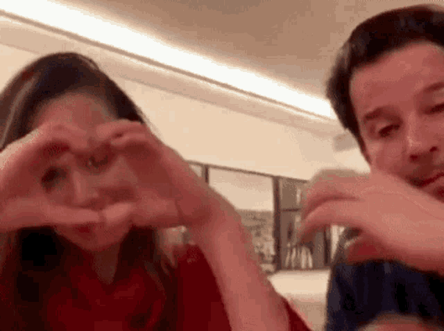 a woman and a man are making a heart shape with their hands .