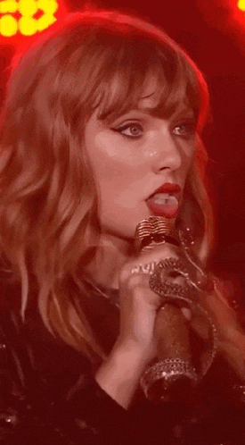 a close up of a woman singing into a microphone with red lights in the background