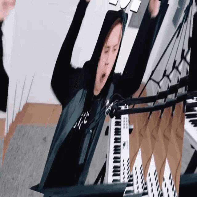 a man in a hoodie is standing in front of a piano keyboard