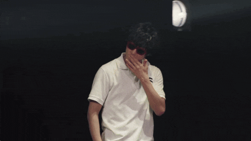 a man wearing sunglasses and a white shirt covering his mouth with his hand