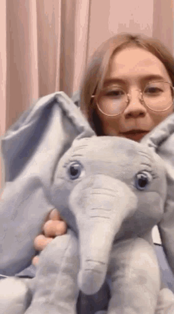 a woman wearing glasses holds a stuffed elephant in her arms