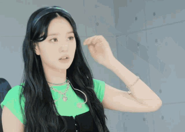 a woman with long black hair wearing a green shirt and black overalls
