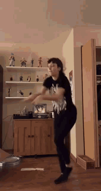 a person is dancing in a living room in front of a shelf with figurines on it .