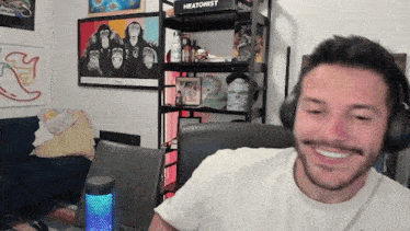 a man wearing headphones is smiling in front of a shelf that says heatonist on it