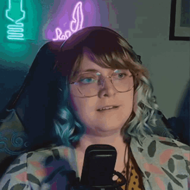 a woman wearing glasses and headphones is sitting in front of a neon sign that says " cool "