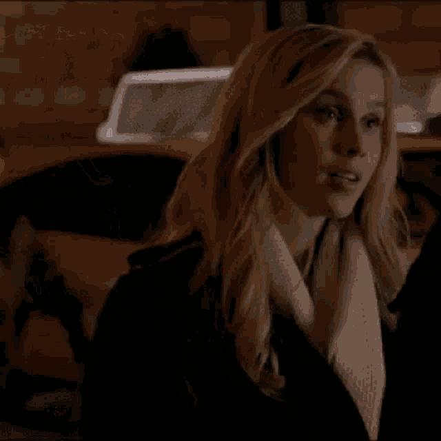 a woman wearing a scarf and a black jacket is standing in front of a car .