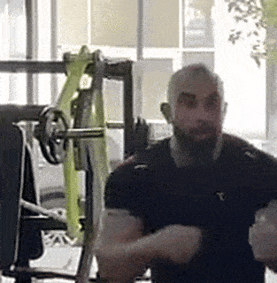 a man with a beard is standing in a gym with a barbell .