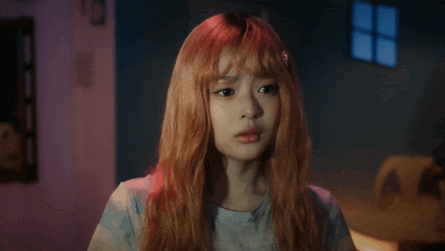 a girl with long red hair is wearing a blue shirt and looking at the camera