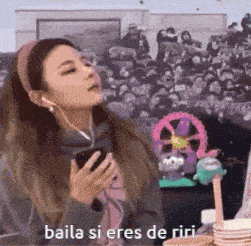 a woman is wearing headphones and holding a cell phone with the words baila si eres de riri below her .