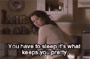 a woman is sitting in a kitchen with a quote that says `` you have to sleep it 's what keeps you pretty ''