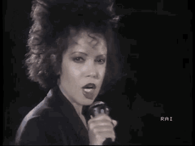 a woman is singing into a microphone in a black and white video .