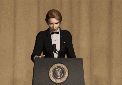 a woman in a tuxedo stands at a podium with the seal of the president of the united states on it