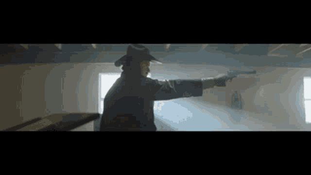 a man in a cowboy hat is holding a gun in a dark room