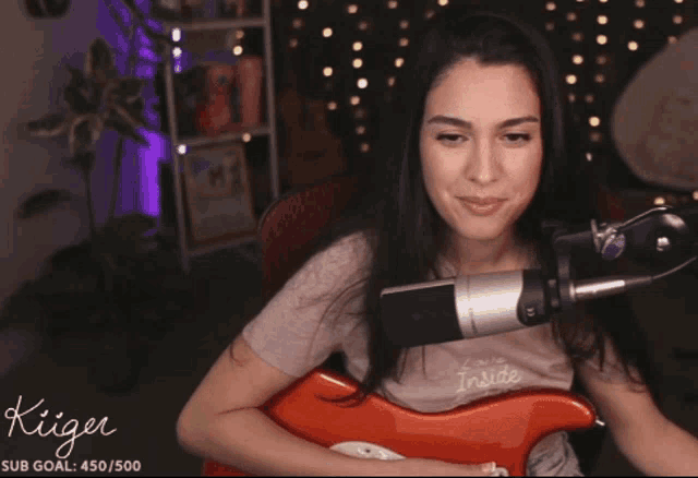 a woman holding a guitar in front of a microphone with the name kiiger on the bottom right
