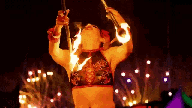 a woman in a crop top is holding two sticks with fire on them