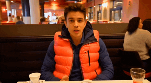 a man in an orange vest sits at a table