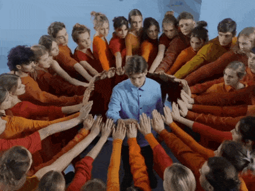 a man in a blue shirt is surrounded by many people in orange shirts