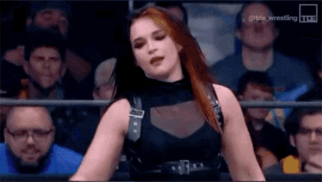 a woman in a black dress is standing in front of a crowd of people in a wrestling ring .