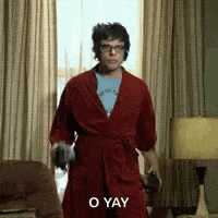 a man in a red robe is standing in a living room holding a pair of glasses .