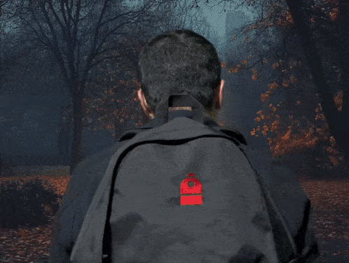 a man wearing glasses and a backpack stands in front of a park with trees and leaves