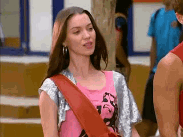 a woman wearing a pink shirt and a red bag is talking to a man .