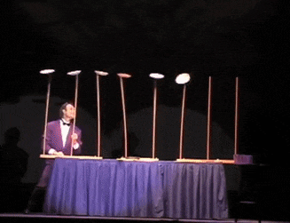 a man in a tuxedo stands on a stage holding a row of sticks