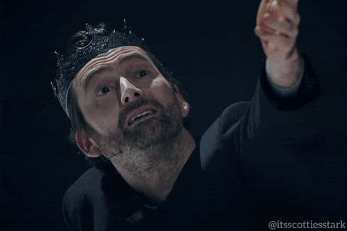 a man with a beard wearing a black crown points his finger at something