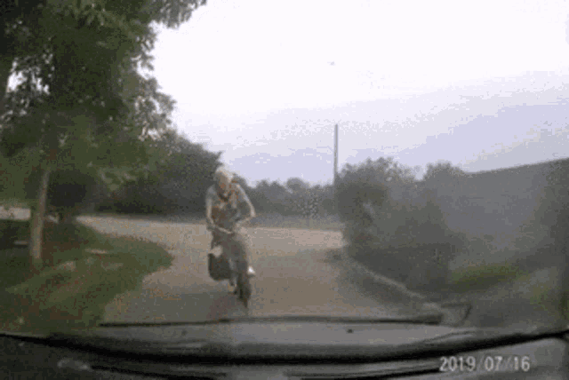 a man is riding a motorcycle down a dirt road in a car windshield .