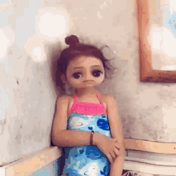 a little girl in a bathing suit is sitting in a corner of a room with her arms crossed .