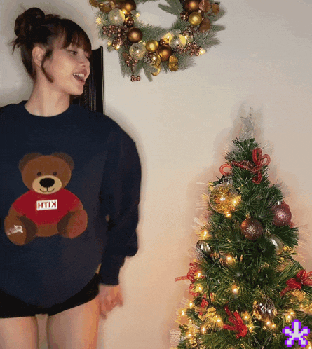 a woman wearing a blue sweater with a teddy bear on it that says kith