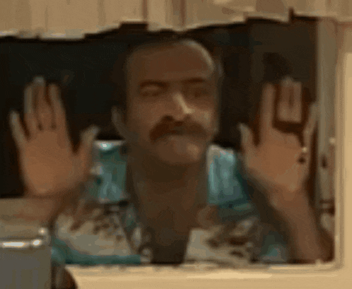 a man with a mustache is looking out of a window and making a funny face .