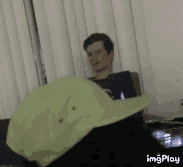 a man is sitting on a couch with a laptop and a green hat on his head .