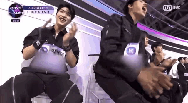a group of young men are sitting on a stage laughing and clapping .