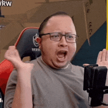 a man wearing glasses is sitting in front of a microphone with his mouth open and making a funny face .