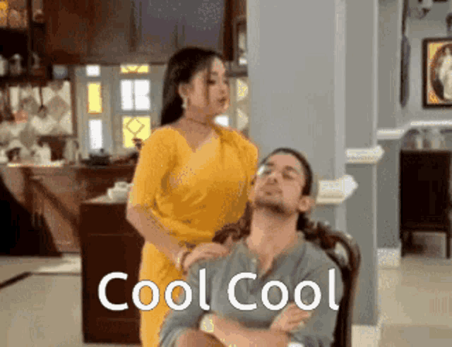 a woman in a yellow saree is standing next to a man in a chair and says cool cool .