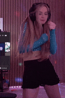 a girl wearing headphones and a blue top is dancing in front of a screen that says continue