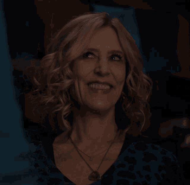 a woman wearing a leopard print shirt and a necklace with a heart on it smiles