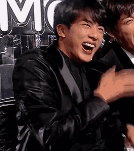 a man in a suit is laughing with his mouth open while standing next to another man .
