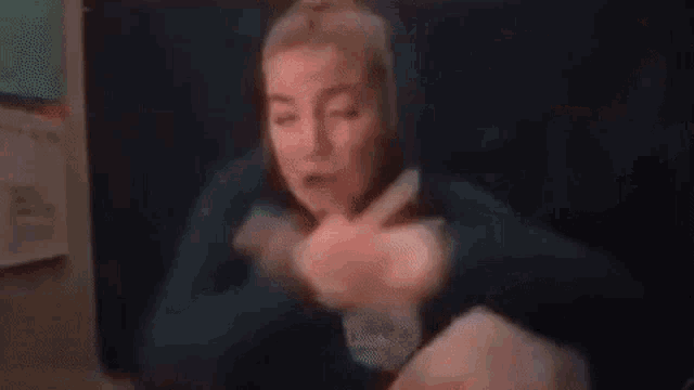 a woman is sitting at a table with her hands on her chest and making a face .