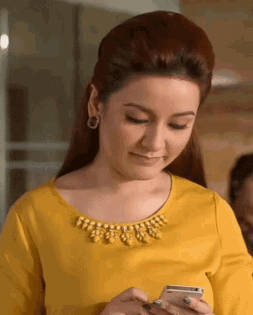 a woman in a yellow top looks at her phone