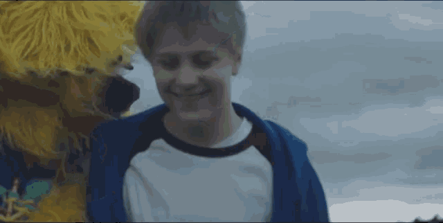 a young boy in a blue jacket is standing next to a yellow stuffed animal
