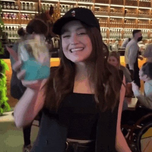 a woman wearing a black hat is holding a blue drink