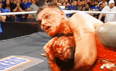 a wrestler is holding another wrestler 's head in a ring with a snickers logo on the floor