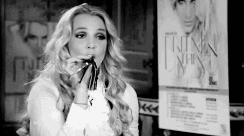 a black and white photo of a woman holding a pencil in her mouth in front of a poster .