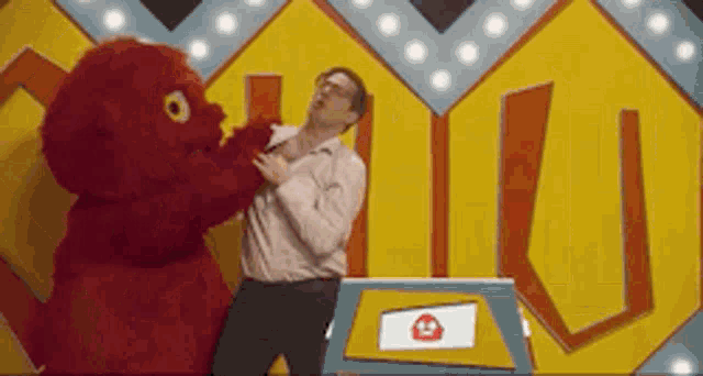 a man is being attacked by a red stuffed animal in front of a sign that says u.