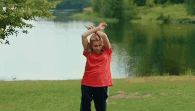 a person in a red shirt is stretching their arms in front of a lake