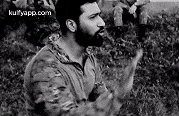 a man with a beard is standing in a field with his hands in the air .