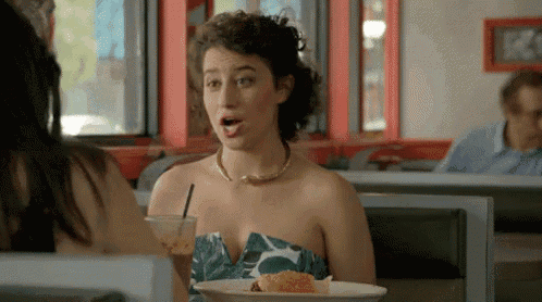 a woman in a dress is sitting at a table with a plate of food and a drink .