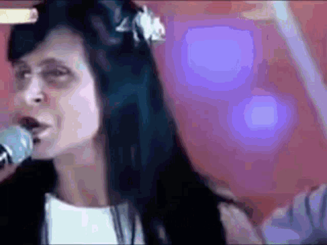 a woman is singing into a microphone with purple lights in the background