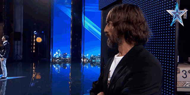 a man with a beard stands in front of a blue wall with a star on it that says ' ugly 72 '